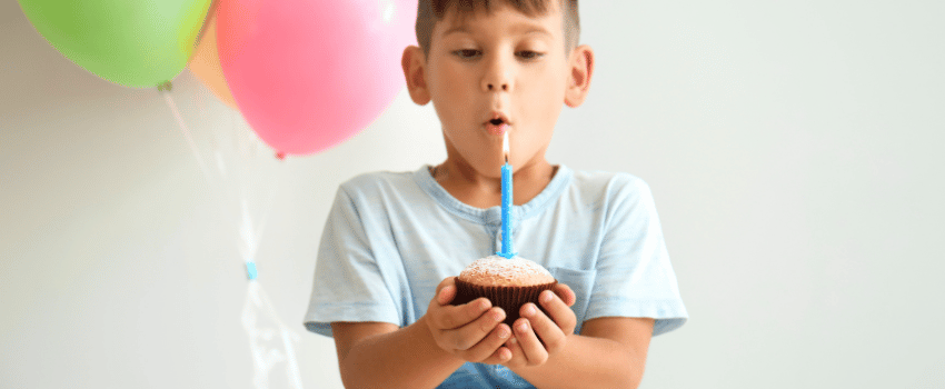 A young boy makes a wish as he blows out a candle on a festive cupcake at a birthday party, enjoying one of the many food birthday freebies available.