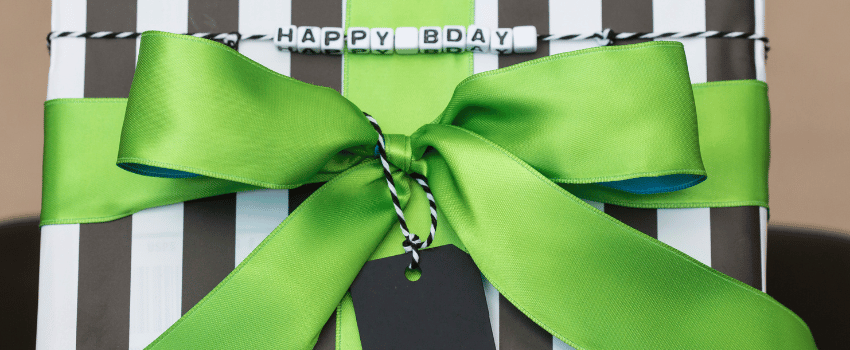 A green ribbon elegantly encircles a black and white striped gift box, symbolizing free birthday gifts.