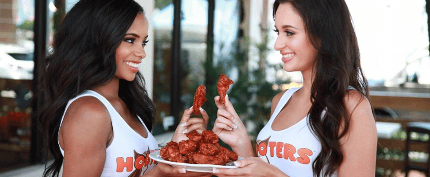 Two happy women in white shirts hold a plate of free 12 wings, celebrating with a Hooters birthday freebie.