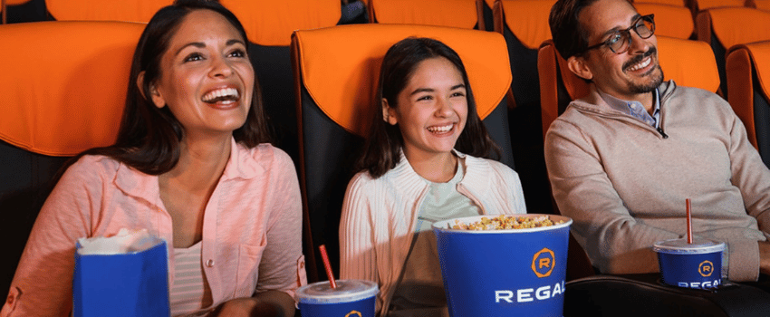 A family sits together in a Regal Movies theater, enjoying free popcorn and drinks. The popcorn is the Regal Movies birthday reward.